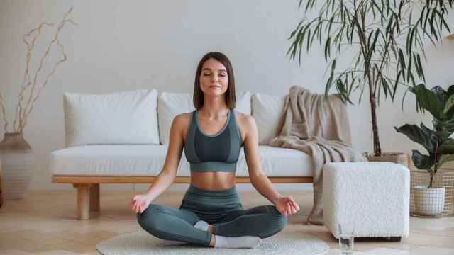 Una mujer joven practica yoga en su casa.