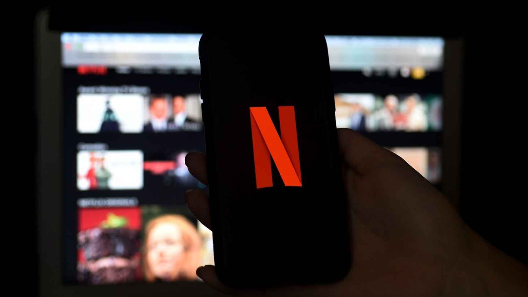 Logo de Netflix en la pantalla de un teléfono móvil frente a un televisor.