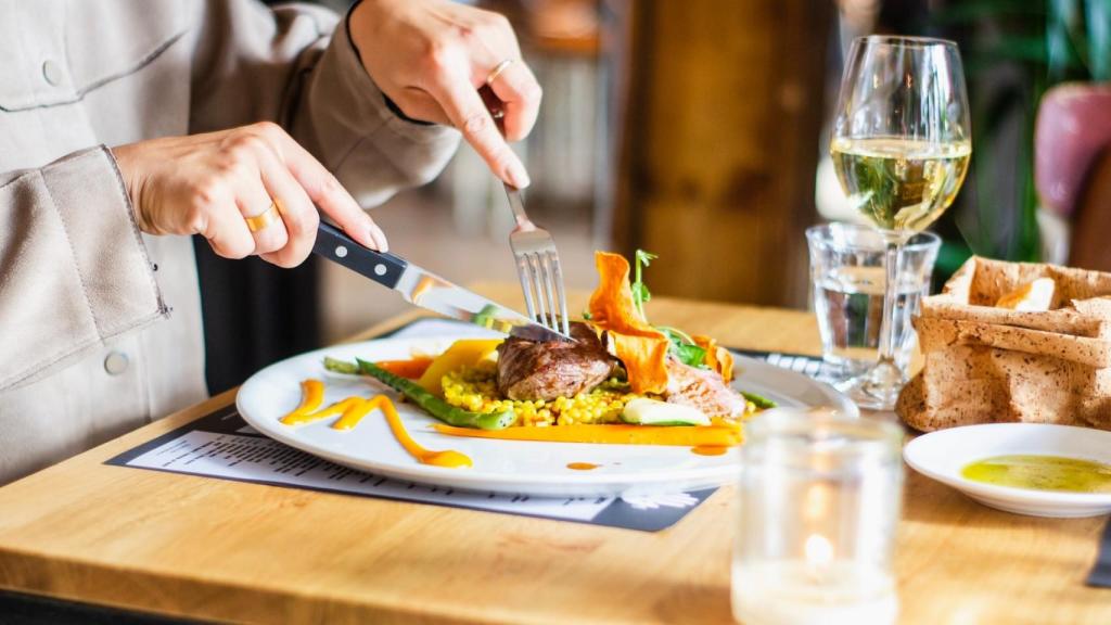 Una persona cenando carne con verduras