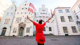 Una mujer posa con una bandera de Letonia frente a un edificio de Riga.