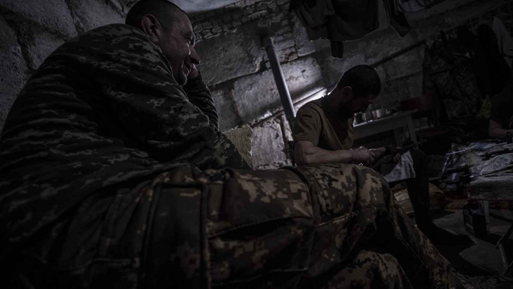 Dos soldados charlan, mientras uno de ellos limpia su armar, en el sótano donde duermen cuando vuelven de misión en el frente de combate de Vuhledar (Donetsk).