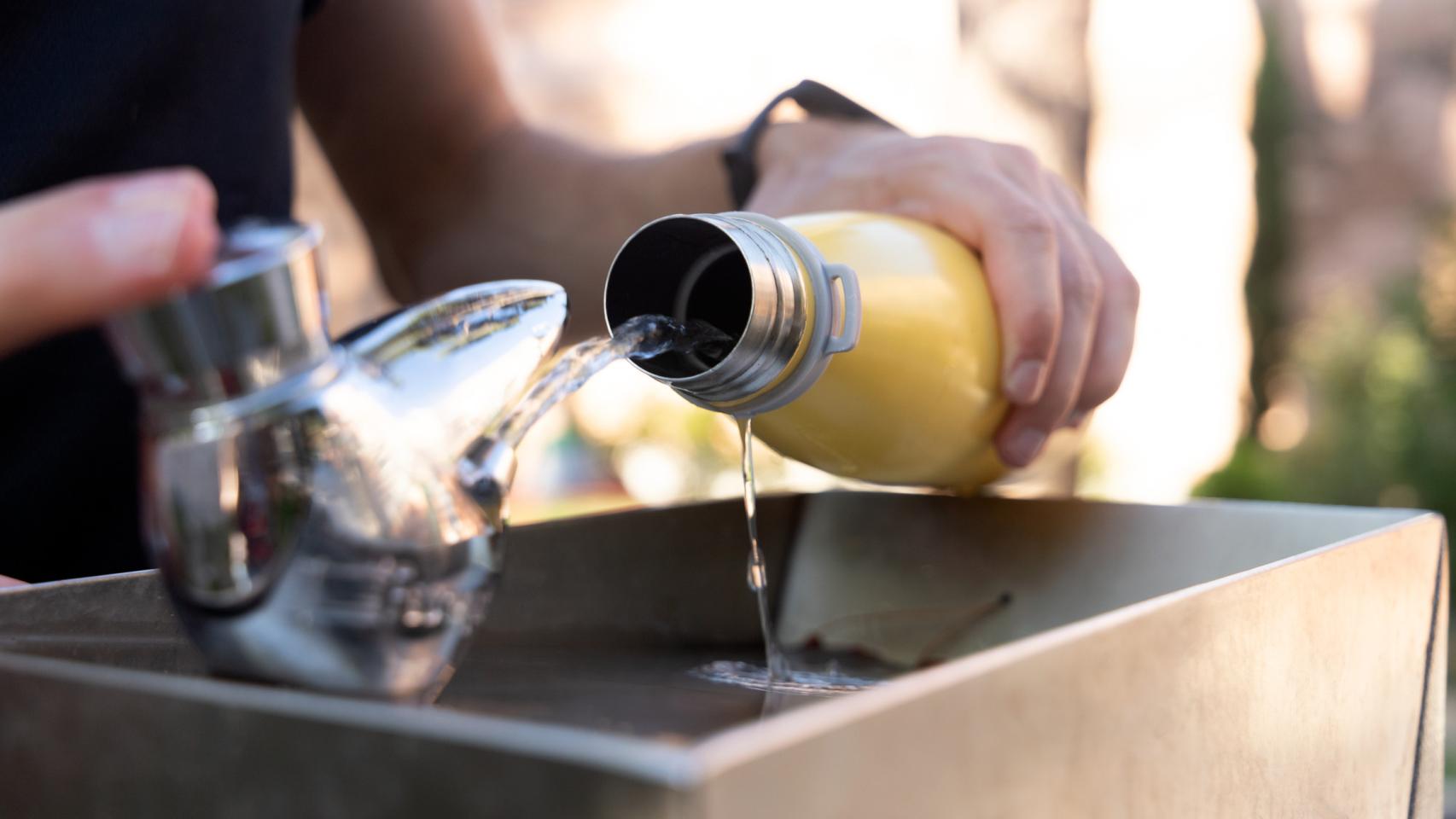 Imagen de archivo de una persona rellanando una botella de metal con agua de una fuente de un parque.