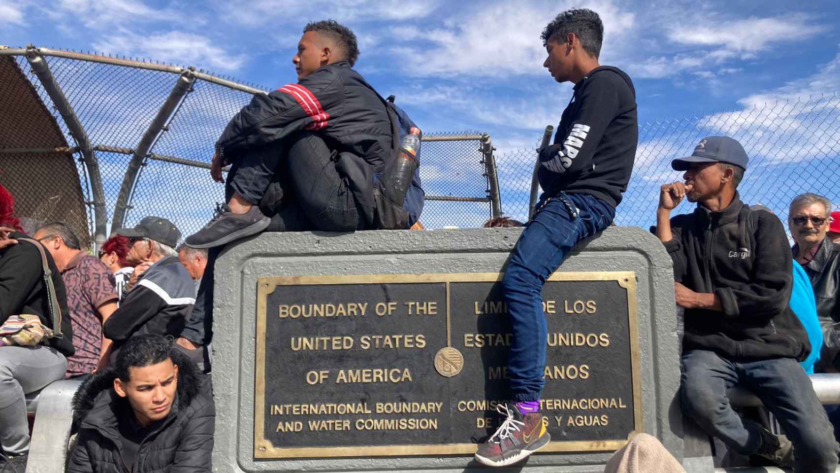 Dos jóvenes se sientan sobre una placa indicativa de la frontera.