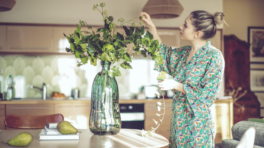 Una mujer en el comedor de su casa coloca las plantas de un  jarrón.