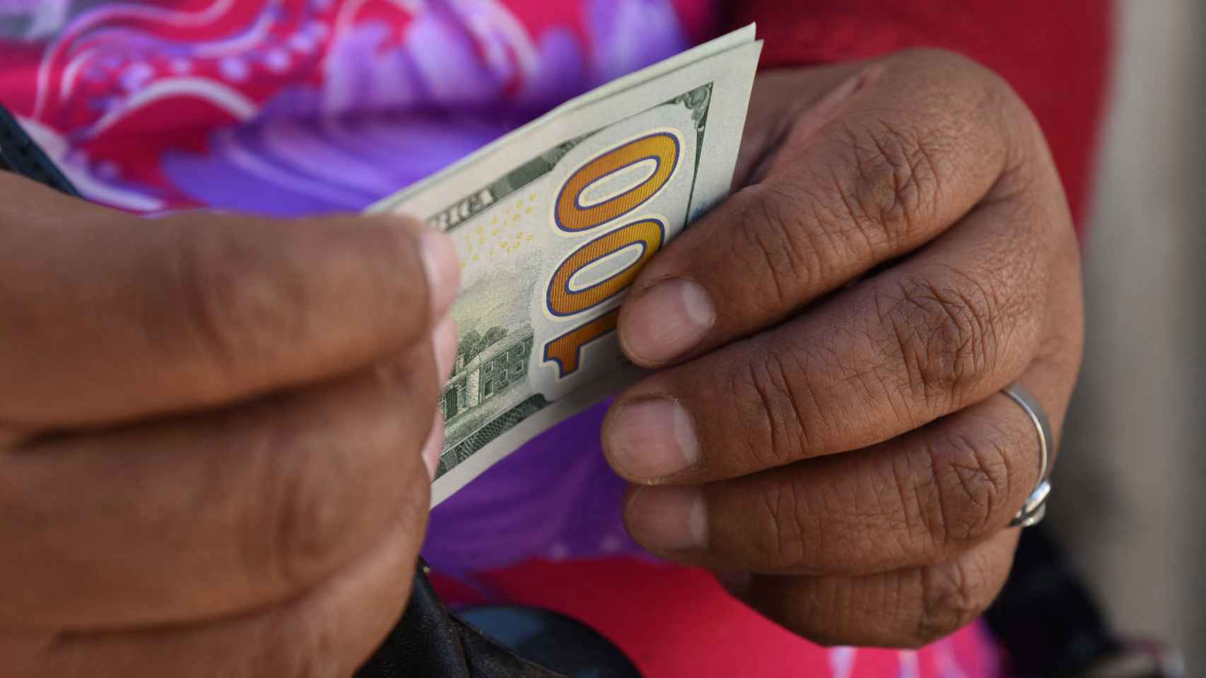 Una mujer sostiene un billete de cien dólares estadounidenses.