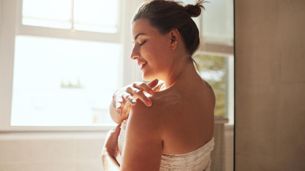 Mujer aplicándose crema en el cuerpo.