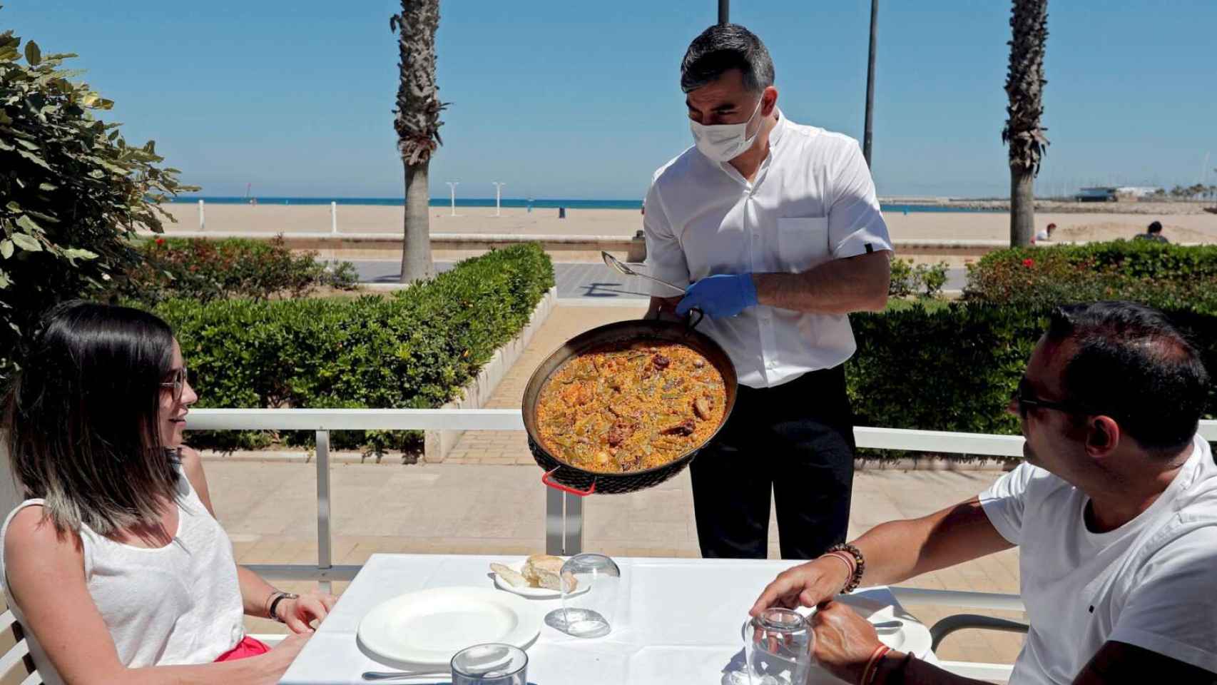 Un camarero sirve una paella en una terraza de la playa de la Malvarrosa de Valencia.