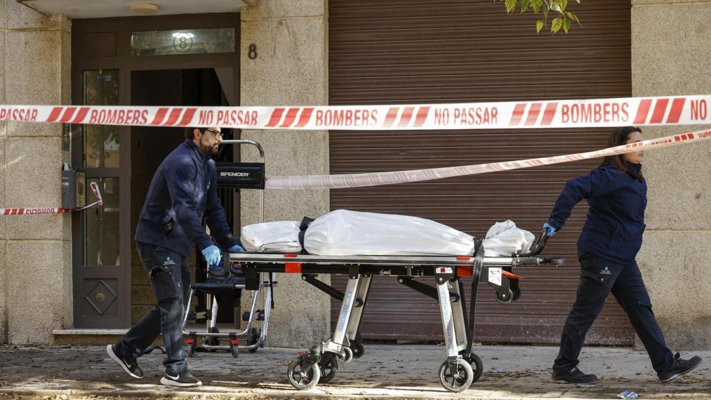 Operarios del retén fúnebre salen con un cadáver del edificio donde se ha declarado el incendio.