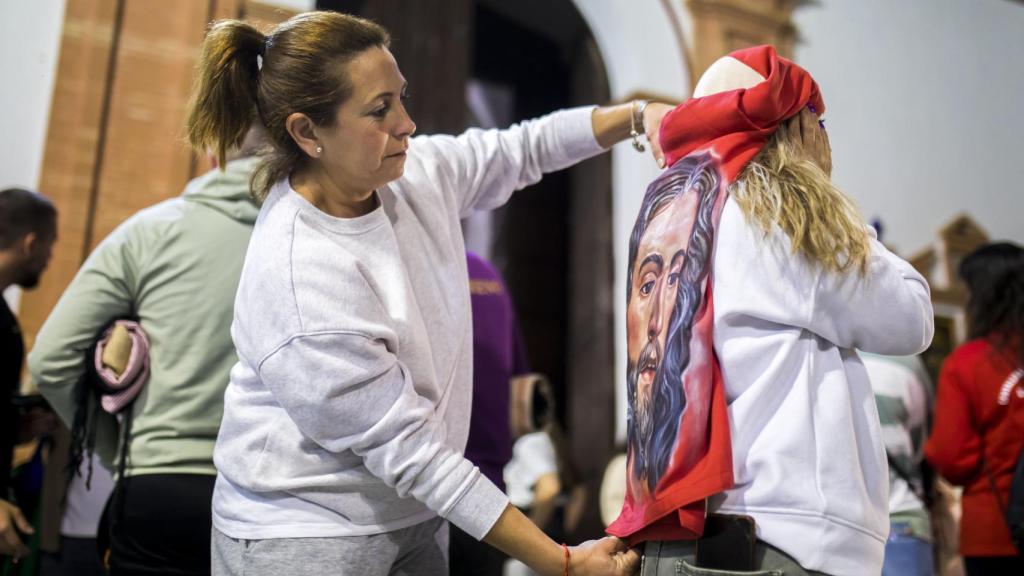 Carmen, una de las costaleras de la hermandad de la Borriquita de Rociana del Condado (Huelva), ayuda a Mari a colocarse el costal.