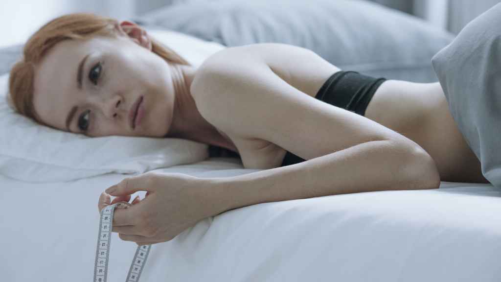 Una adolescente triste tumbada en la cama con un metro en la mano.