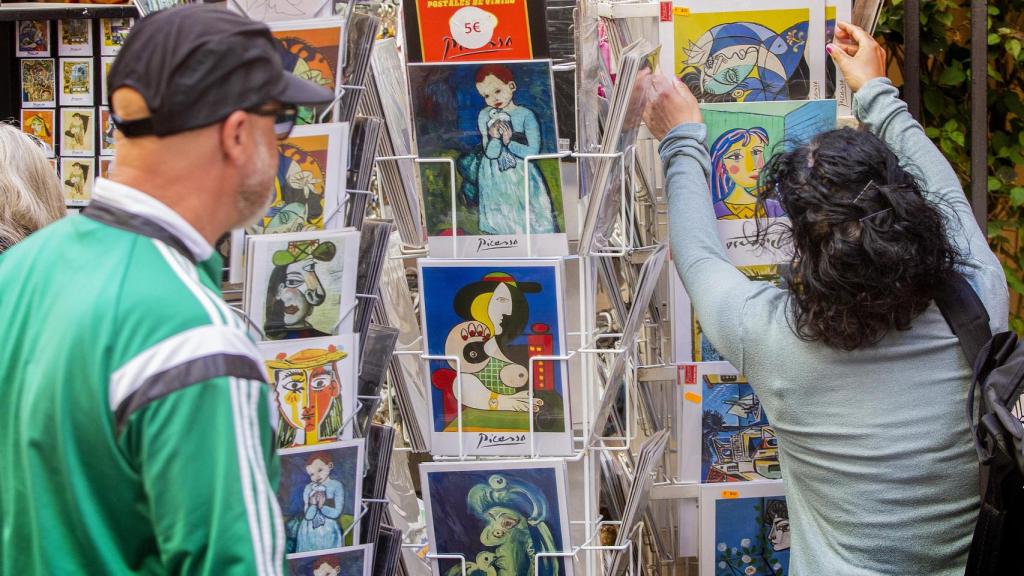 Unos turistas miran postales con obras del pintor Pablo Ruiz Picasso en el entorno del museo que lleva su nombre en el centro de Málaga en el día del 50 aniversario del fallecimiento del artista, este sábado.