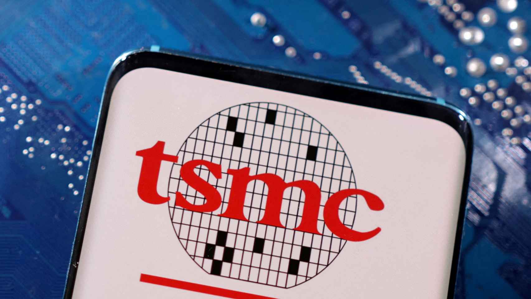 Logo de la compañía de semiconductores TSMC en la pantalla de un teléfono móvil delante de un chip.