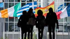 Varios jóvenes caminan entre banderas de países miembros de la Unión Europea, en Bruselas.