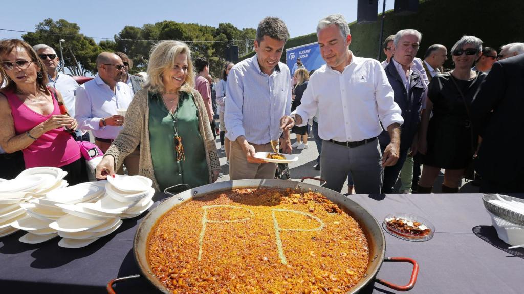 La diputada nacional Macarena Montesinos, el candidato valenciano del PP, Carlos Mazón y el Coordinador nacional del PP, Elías Bendodo, sirven paella con las siglas del PP durante un momento del mitin del PP de Alicante.