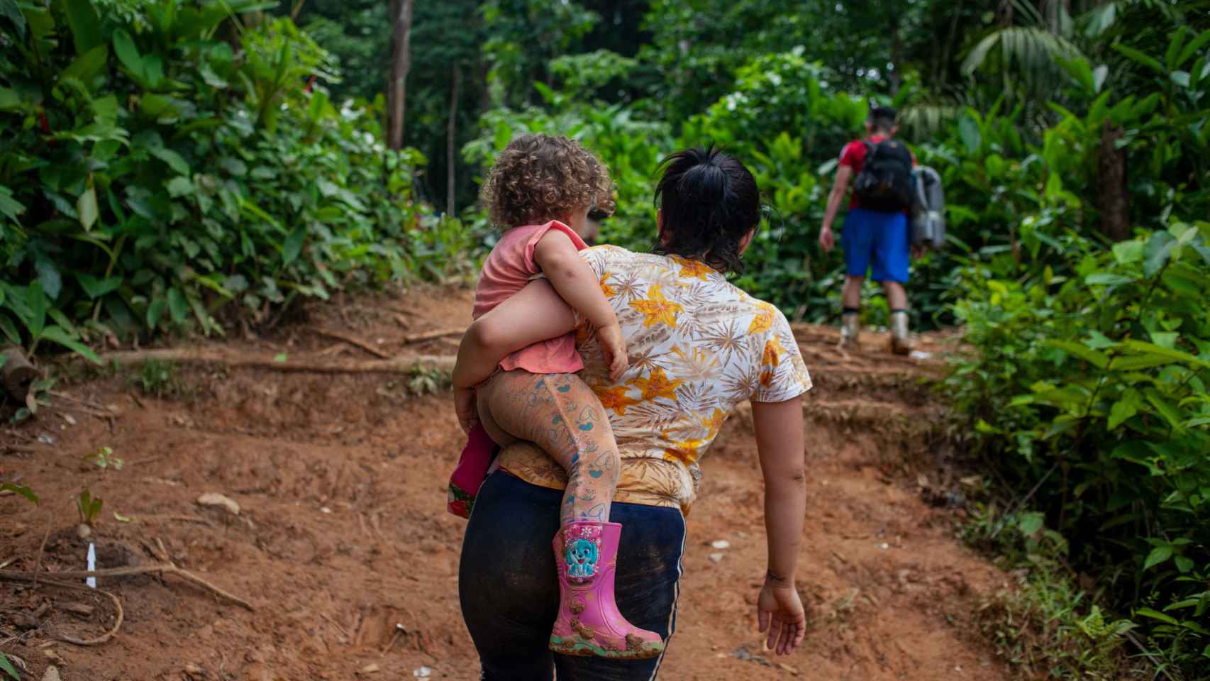 Una mujer venezolana camina por el sendero selvático del Darién con su hija en brazos.