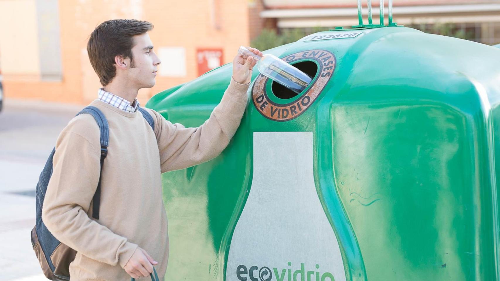 Un joven deposita un envase de vidrio en el contenedor verde