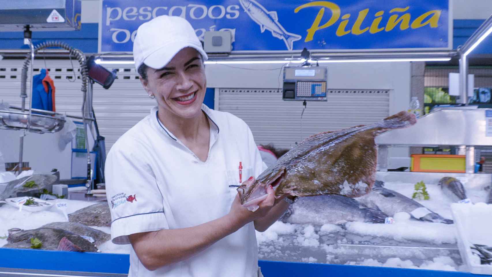 Piliña posa con un rodaballo frente a su puesto de pescado en la Praza de Abastos de Portonovo