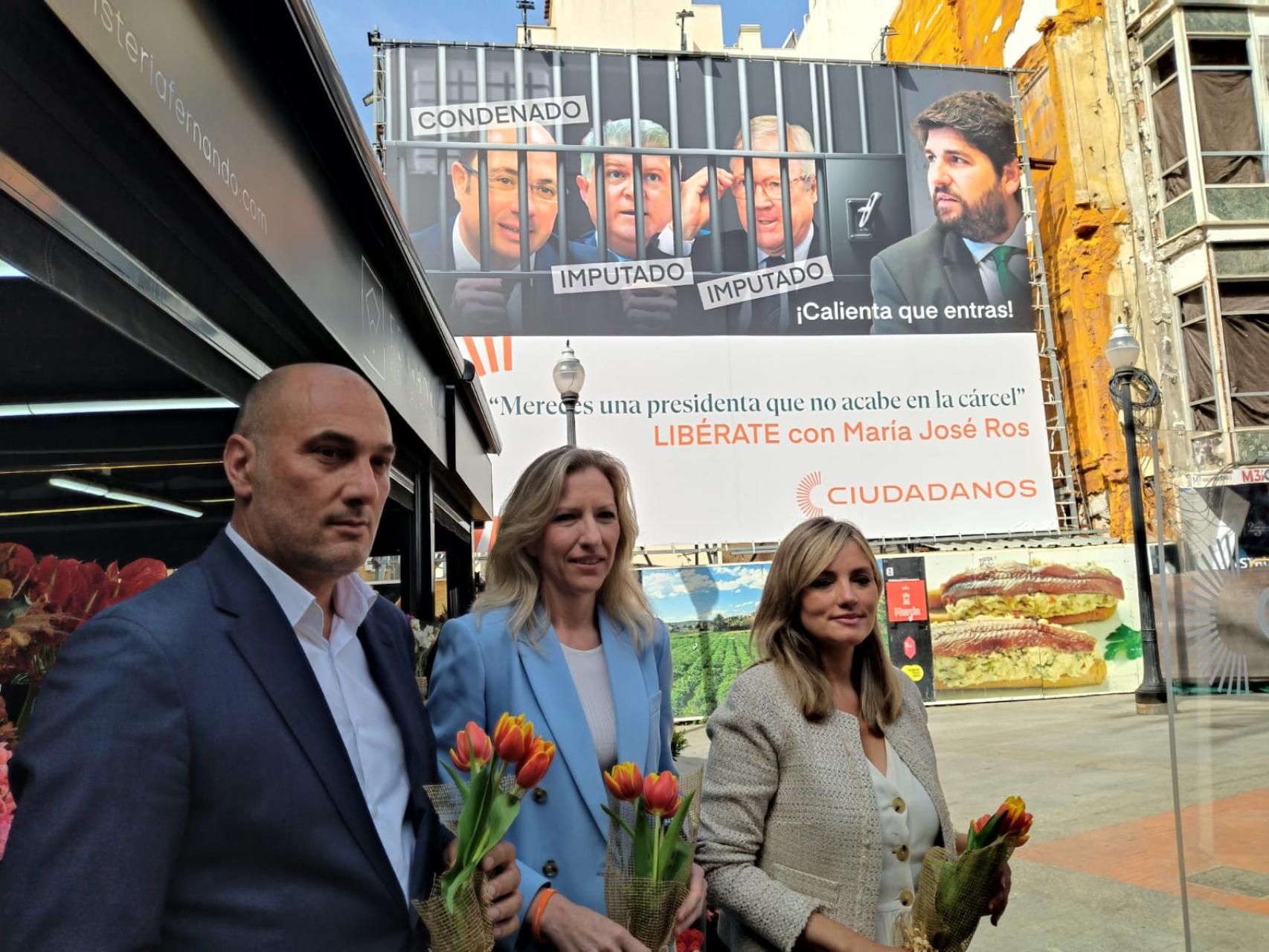 El candidato por Cs a la alcaldía de Murcia, Pedro García Rex, la candidata por Cs a la presidencia de la Región de Murcia, María José Ros, y la portavoz nacional de Ciudadanos, Patricia Guasp, este viernes, posando con la lona que han colocado los naranjas en la plaza de las Flores de Murcia.