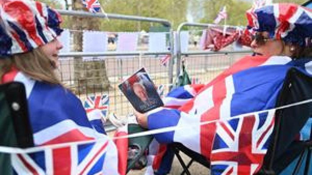 .- Los fanáticos reales leen un libro sobre el rey Carlos mientras esperan en la ruta de la procesión de coronación en The Mall en Londres, Gran Bretaña, el 05 de mayo de 2023.