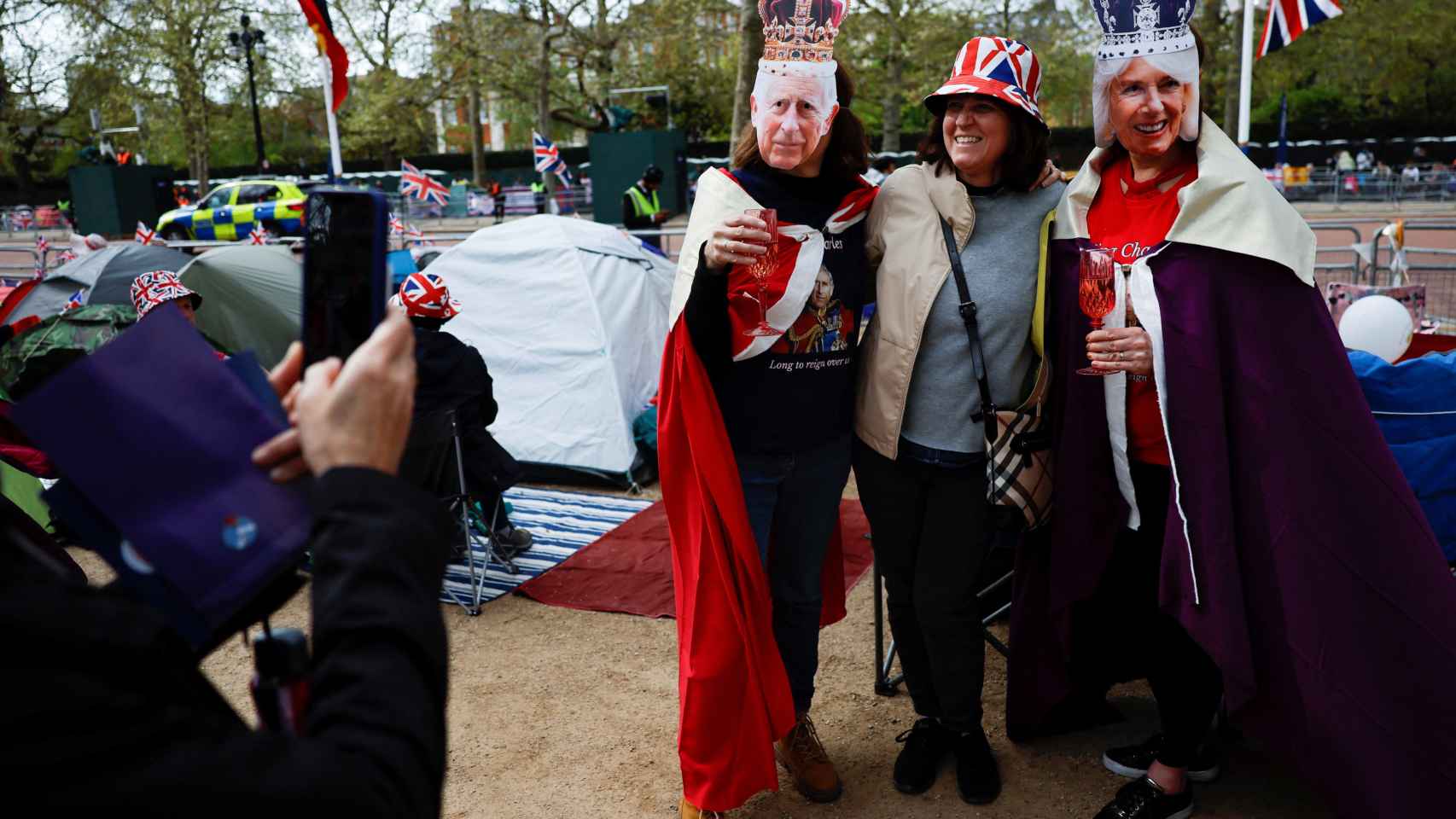 Una mujer haciéndose un foto con dos personas con las máscaras de Carlos III de Inglaterra y la reina consorte Camilla en los alrededor de Buckingham Palace.