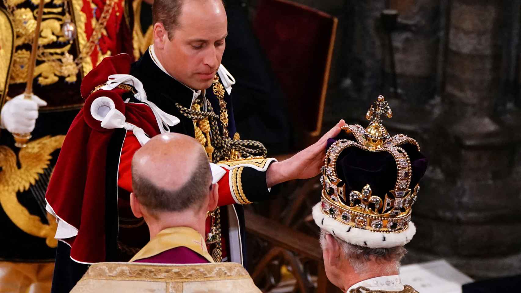 el príncipe Guillermo toca la corona de San Eduardo que porta su padre, Carlos III.