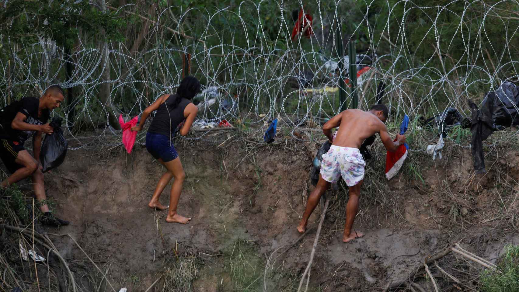Un grupo de migrantes intenta escalar una valla tras cruzar el río Bravo, este miércoles.
