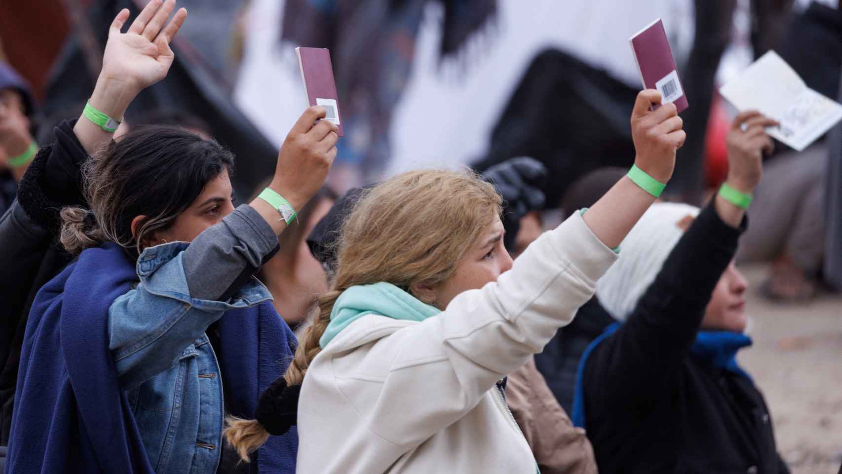 Dos mujeres alzan sus pasaportes ante la policía fronteriza estadounidense.