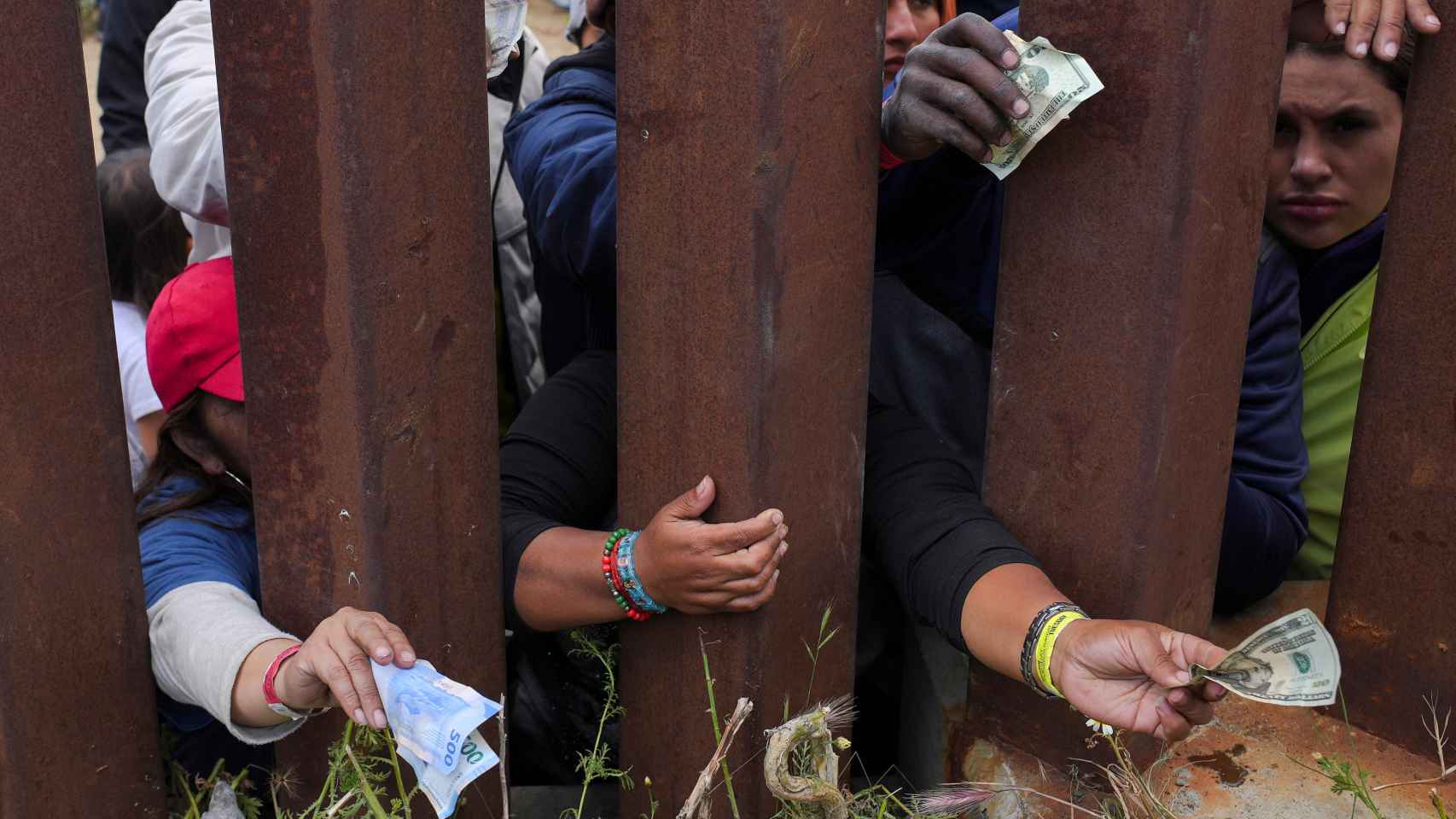 Migrantes cuelan billetes para pagar a un repartidor de comida a domicilio que ha acudido hasta la frontera.