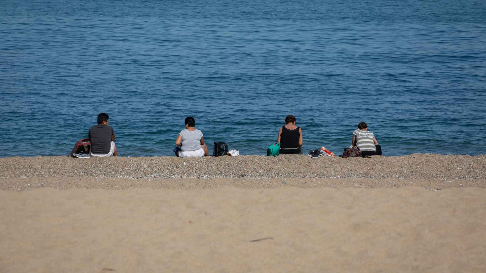 arias personas sentadas en la Playa de la Barceloneta.