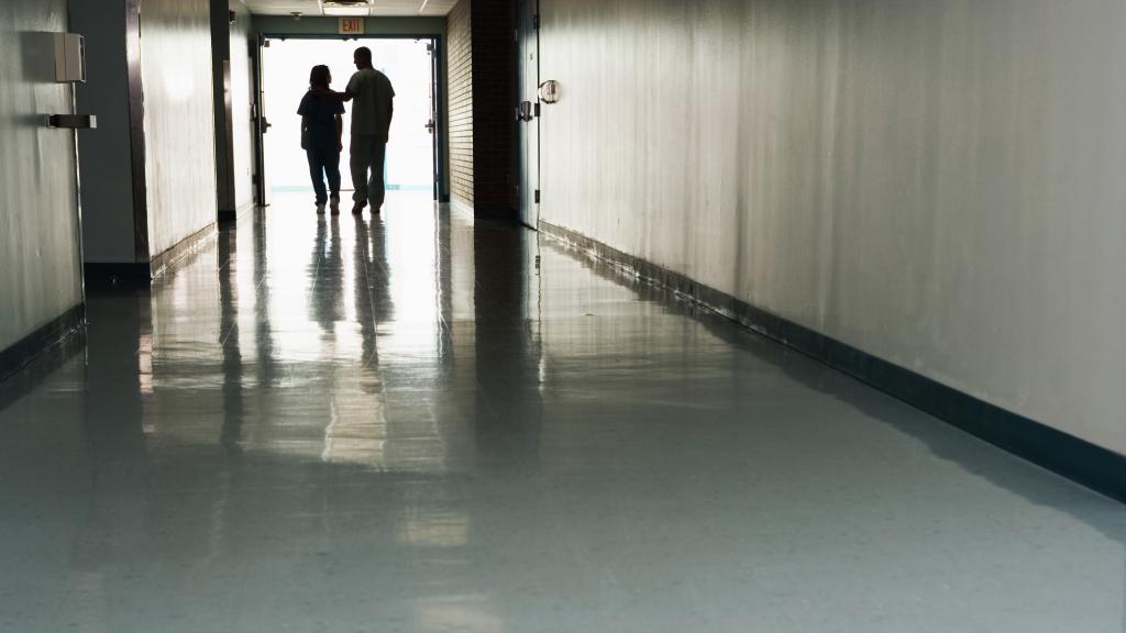 Dos personas caminan por un pasillo de hospital.
