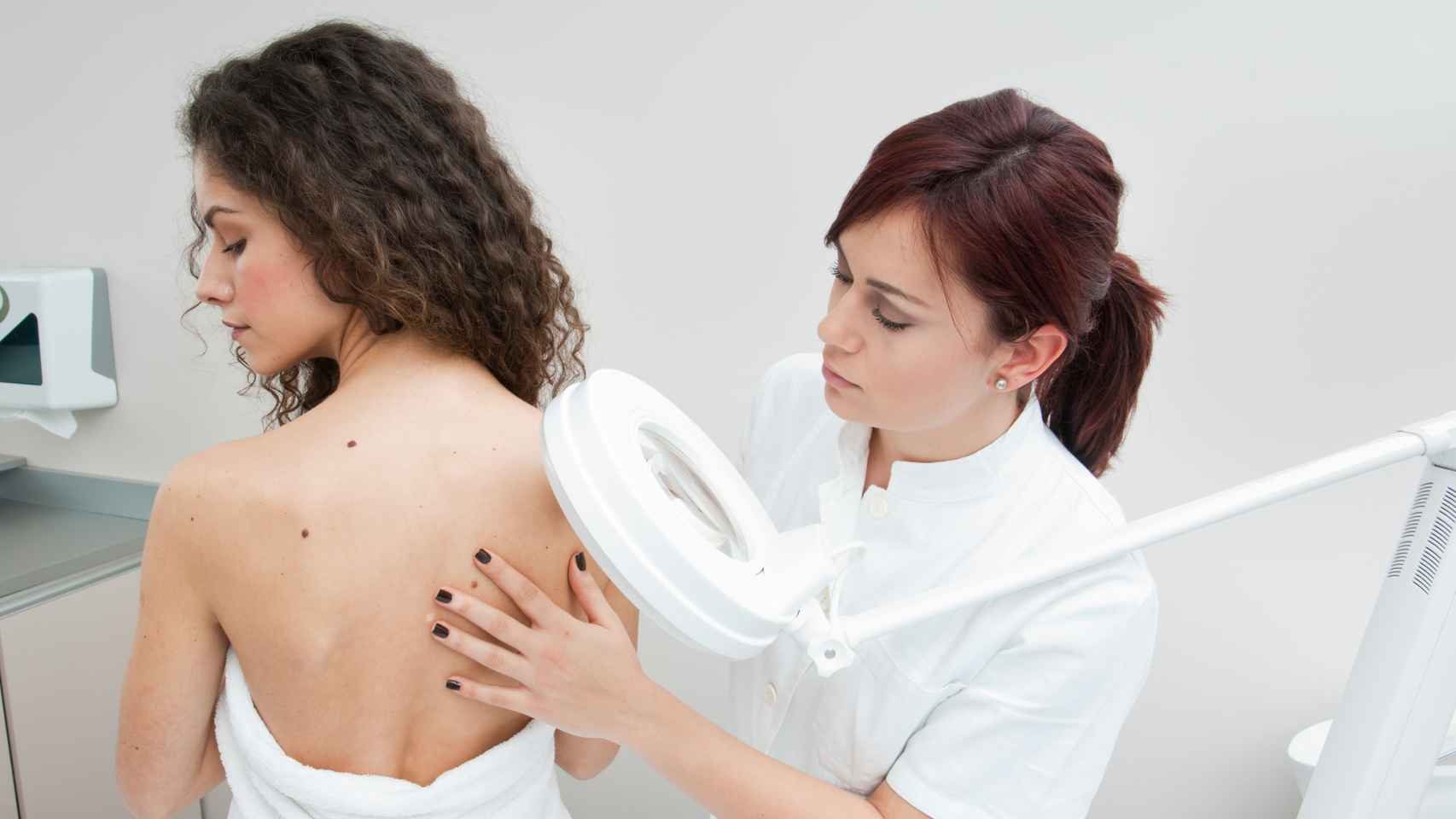 Una dermatóloga examina la piel de una mujer.