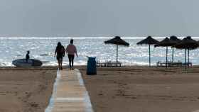 Dos personas caminan por una pasarela de madera en una playa valenciana, hace unas semanas.