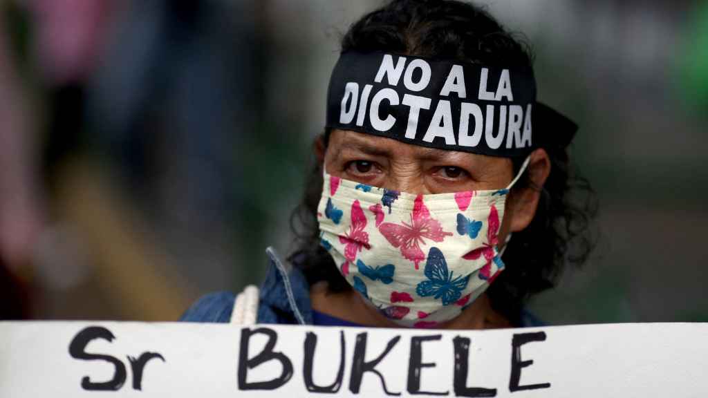 Una manifestante lleva una cinta con el mensaje No a la dictadura y soporta una pancarta contra Bukele.