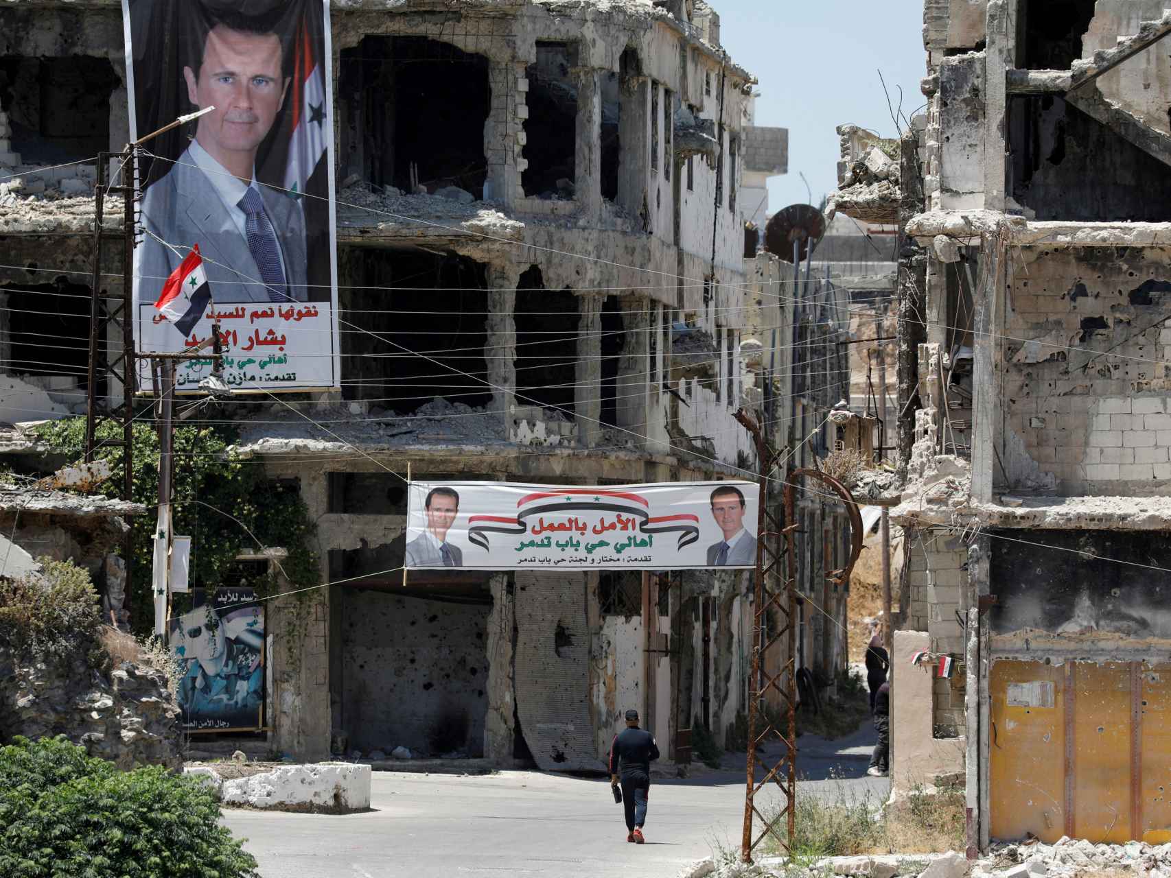 Un hombre pasa junto a pancartas que representan al presidente de Siria, Bashar al-Assad, en Homs, Siria.