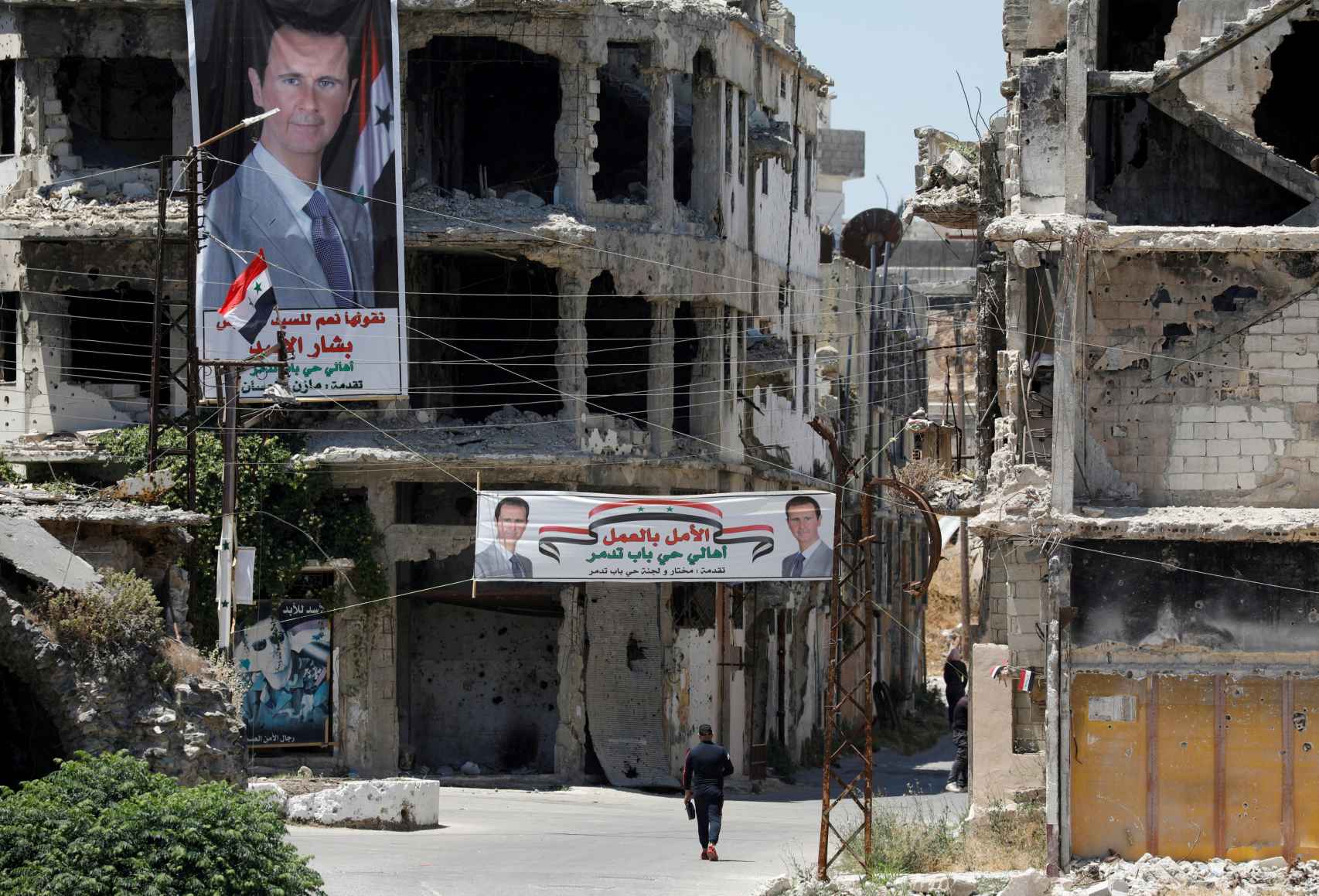 Un hombre pasa junto a pancartas que representan al presidente de Siria, Bashar al-Assad, cerca de edificios dañados, antes de las elecciones presidenciales del 26 de mayo, en Homs, Siria, el 23 de mayo de 2021.
