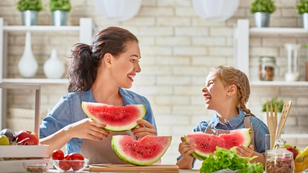 Madre e hija disfrutan de una porción de sandía en la cocina.