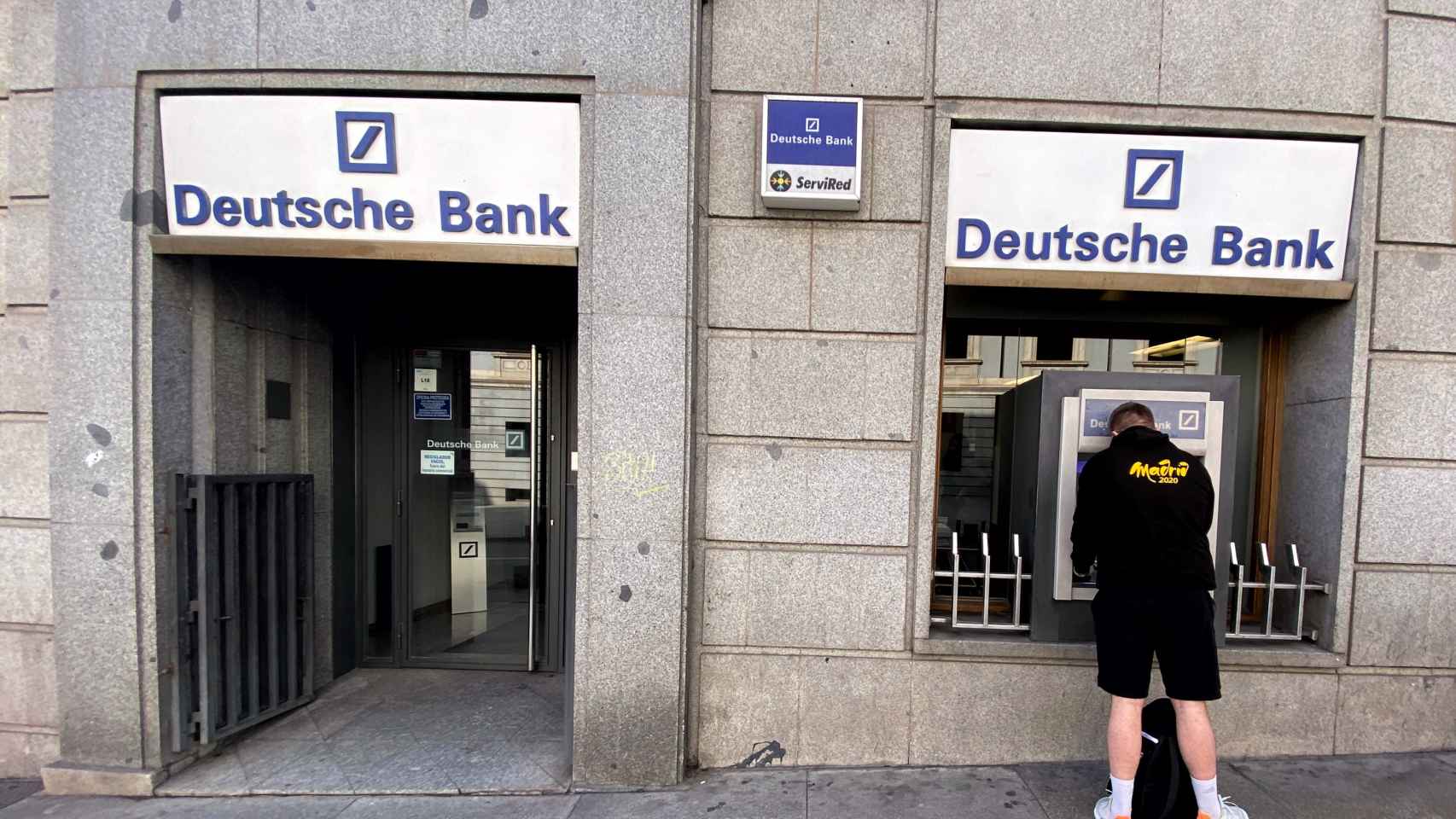 Un hombre retira dinero de un cajero de Deutsche Bank.