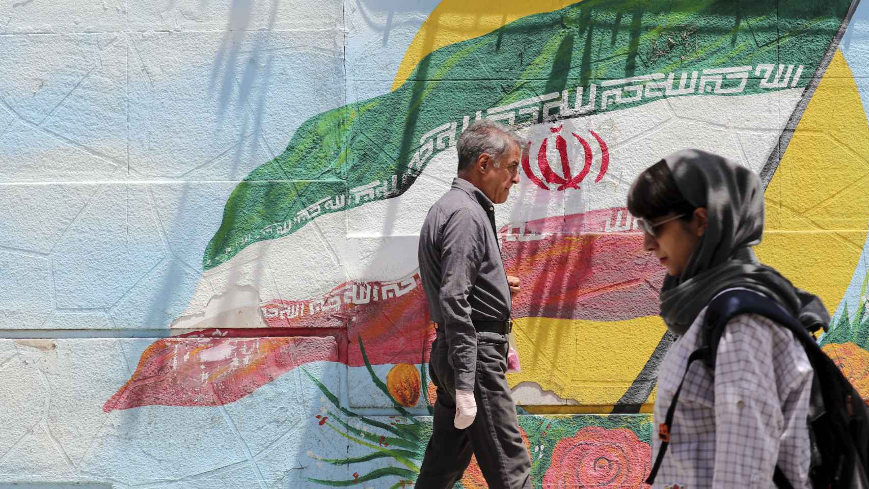 Dos iraníes caminan junto a un mural con la bandera nacional, el en 12 de junio en Teherán.