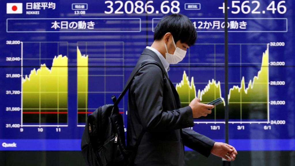 Un hombre camina delante de una pantalla en la que aparece la cotización del Nikkei.