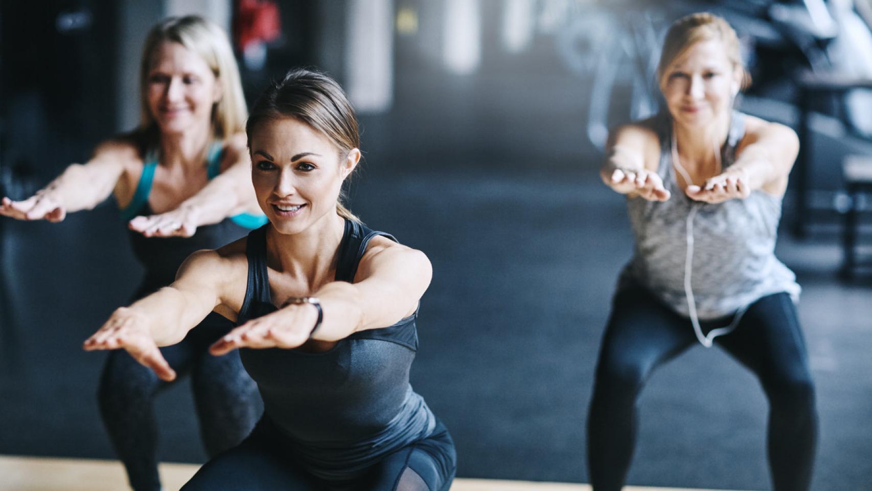 Mujeres haciendo sentadillas en gimnasio.