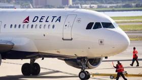 Un avión de la empresa Delta controlado por operarios en la pista de aterrizaje