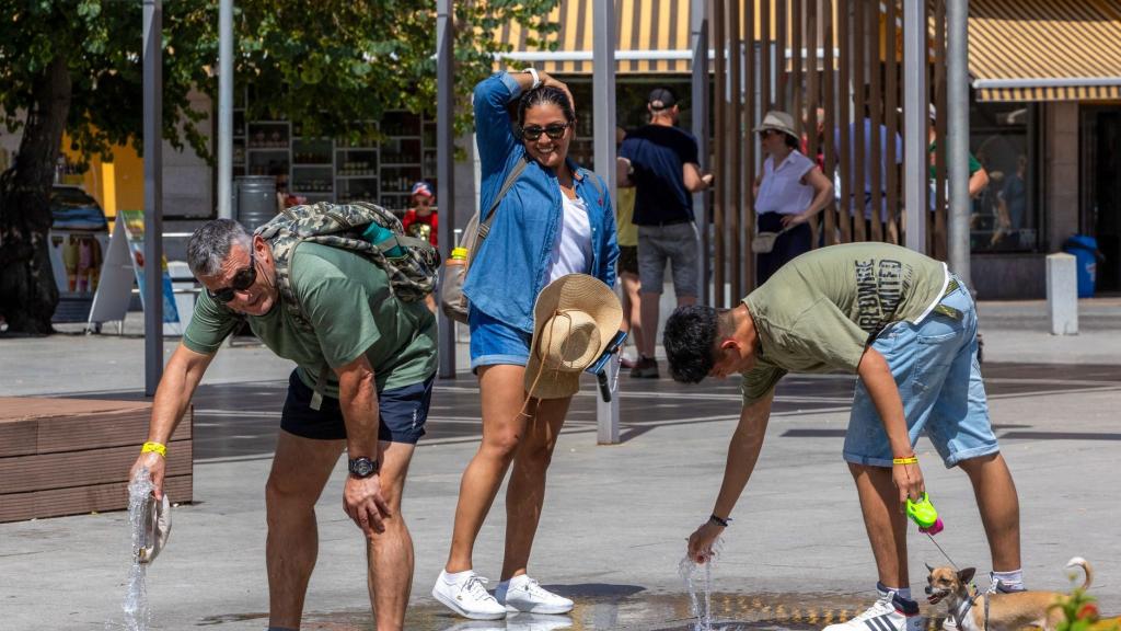 Varias personas se refrescan en una fuente.