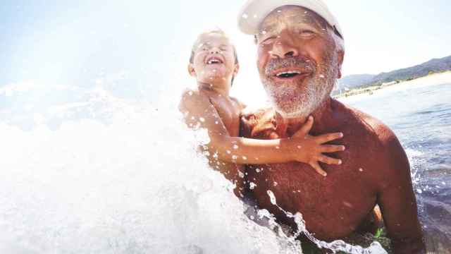 Un abuelo con gorra en la playa con su nieto.