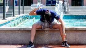 Un joven trata de refrescarse con agua de una fuente durante una ola de calor en Madrid.