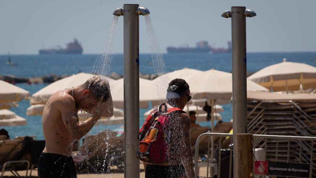 Varias personas se mojan en las duchas de playa.