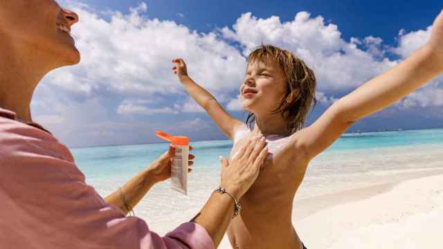 Una mujer aplicando crema protectora a su hijo en la playa.