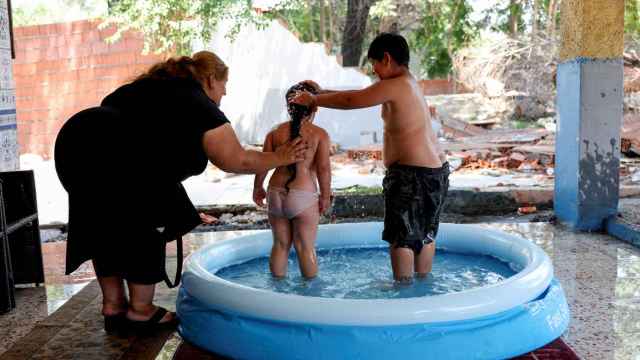 Una mujer gitana baña a dos niños en una piscina hinchable en la Cañada Real (Madrid).