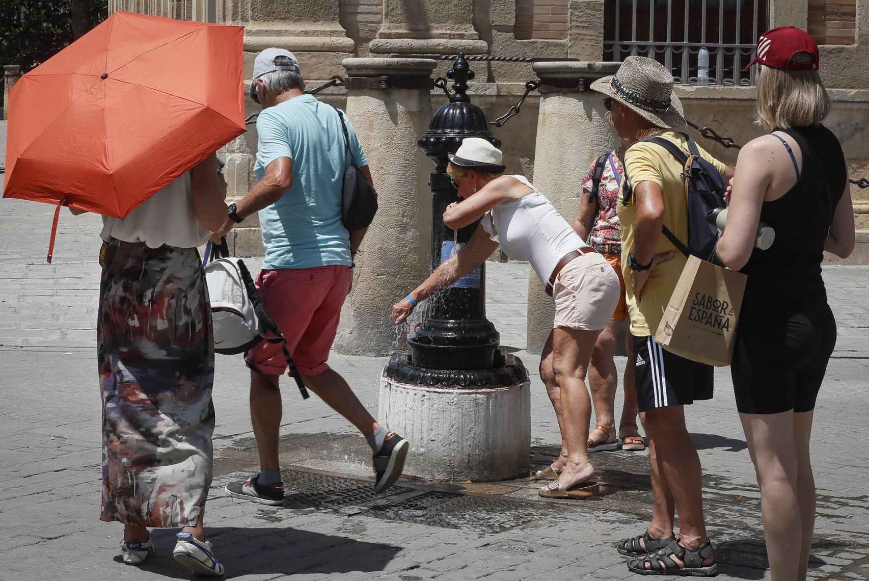 Varias personas se refrescan en fuentes del centro de Sevilla.