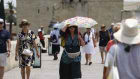 Una mujer se cubre del sol con una sombrilla en el Puente Romano de Córdoba.