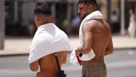 Varios jóvenes caminan por el centro de Málaga con toallas al cuello.